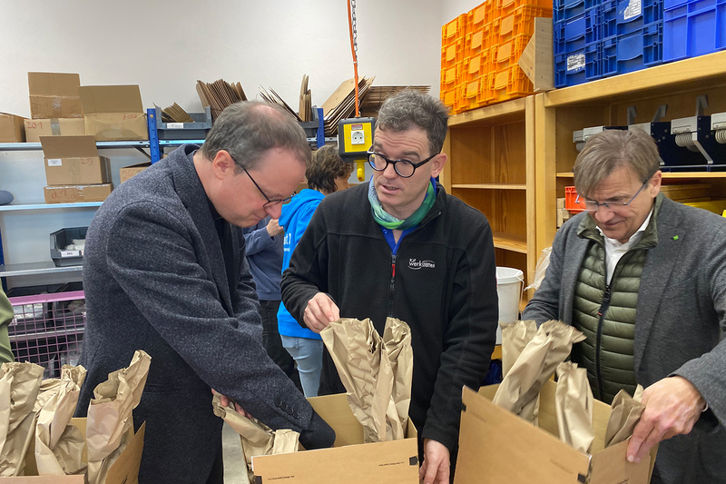 Domkapitular Michael Dreßel (l.), der Vorsitzende der KJF,  und KJF-Direktor Michael Eibl (r.) unterstützten die Mitarbeiterinnen und Mitarbeiter der KJF Werkstätten beim Päckchen packen. (Foto: Sebastian Schmid)