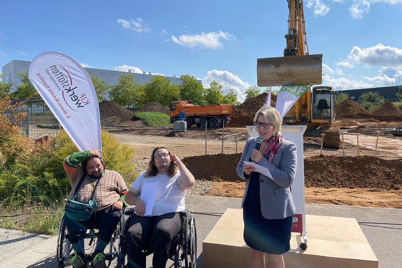 Melanie Eibl, Johannes Gutekunst und ein weiterer Mitarbeiter der Werkstätten stehen vor der Baustelle des Erweiterungsbaus.