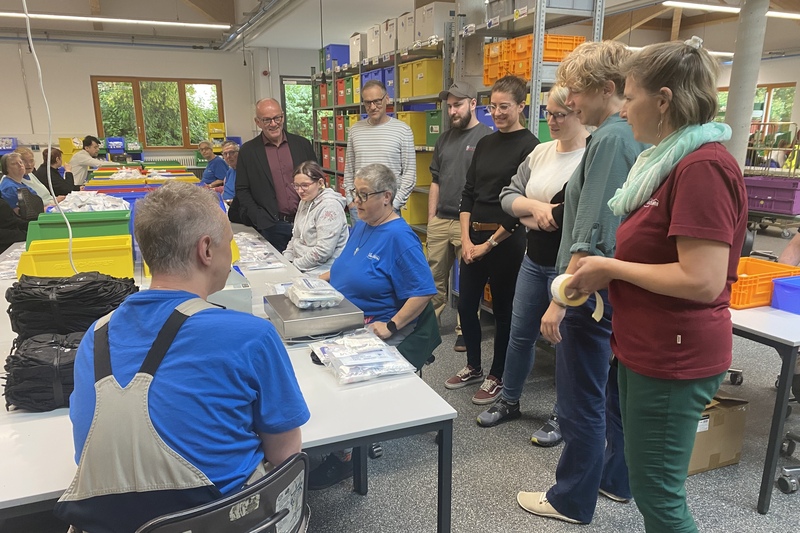 Mitarbeiter der Werkstättte und die Teilnehmer der Aktion Schichtwechsel unterhalten sich in der Montageabteilung. 