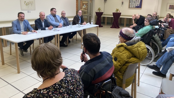 Politiker sitzen vor den Gästen der Podiumsdiskussion. Ein Mitarbeiter der KJF Werkstätten stellt ihnen eine Frage.